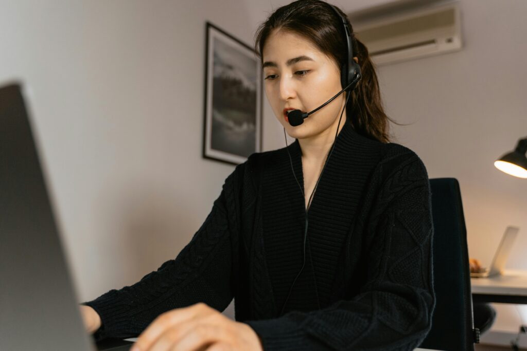 A woman working in a call center, using a laptop and headset for customer service assistance.